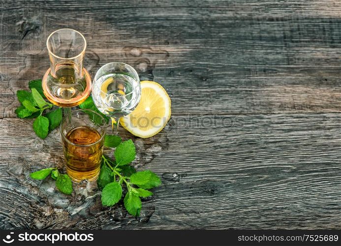 Alcoholic drinks with ice, lemon, mint leaves on wooden background. Food beverages