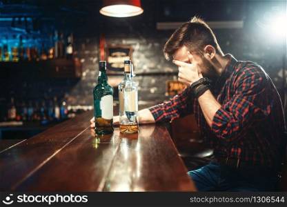 Alcoholic sitting at the bar counter and drinks strong alcohol beverages. Male person in pub, alcoholism, drunkenness