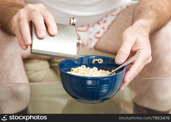 Alcoholic spiking his cereal with vodka from a flask. Shallow depth of field with focus on the pouring alcohol.