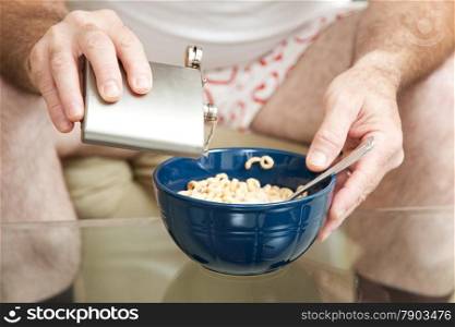 Alcoholic spiking his cereal with vodka from a flask. Shallow depth of field with focus on the pouring alcohol.