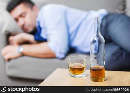 alcoholism, alcohol addiction and people concept - bottle with glass of whiskey on table and sleeping drunk man. bottle of alcohol on table and sleeping drunk man. bottle of alcohol on table and sleeping drunk man