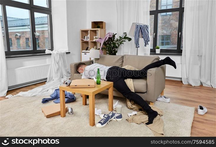 alcoholism, alcohol addiction and people concept - drunk man sleeping on sofa in messy room at home. drunk man sleeping on sofa in messy room at home