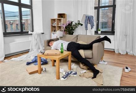 alcoholism, alcohol addiction and people concept - drunk man sleeping on sofa in messy room at home. drunk man sleeping on sofa in messy room at home