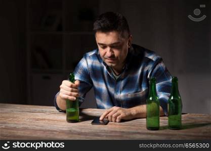 alcoholism, alcohol addiction and people concept - drunk man with smartphone and bottle of beer at night. man with smartphone and bottle of beer at night