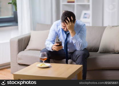 alcoholism, alcohol addiction and people concept - drunk man with smartphone and glass of brandy at home. drunk man with smartphone and alcohol at home