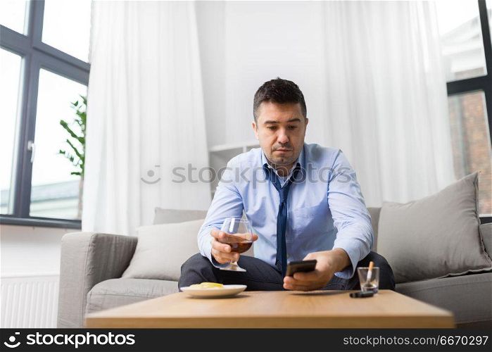 alcoholism, alcohol addiction and people concept - drunk man with smartphone and glass of brandy at home. drunk man with smartphone and alcohol at home. drunk man with smartphone and alcohol at home