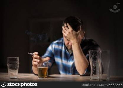 alcoholism, alcohol addiction and people concept - male alcoholic drinking beer and smoking cigarette at night. drunk man drinking alcohol and smoking cigarette. drunk man drinking alcohol and smoking cigarette