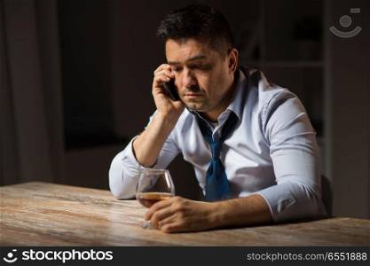 alcoholism, alcohol addiction and people concept - male alcoholic drinking brandy and calling on smartphone at night. man with alcohol calling on smartphone at night. man with alcohol calling on smartphone at night