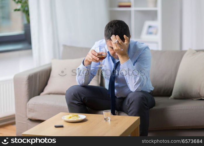 alcoholism, alcohol addiction and people concept - male alcoholic drinking brandy and smoking cigarette at home. drunk man drinking alcohol and smoking cigarette