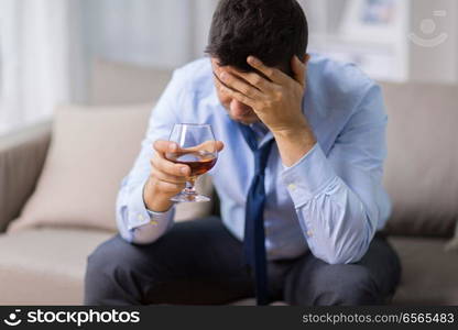 alcoholism, alcohol addiction and people concept - male alcoholic drinking brandy at home. drunk man with glass of alcohol at home