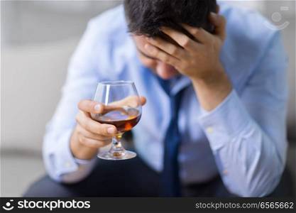 alcoholism, alcohol addiction and people concept - male alcoholic drinking brandy at home. drunk man with glass of alcohol at home