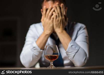alcoholism, alcohol addiction and people concept - male alcoholic drinking brandy on table at night. drunk man with glass of alcohol on table at night. drunk man with glass of alcohol on table at night
