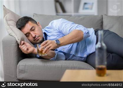 alcoholism, alcohol addiction and people concept - male alcoholic lying on sofa and drinking whiskey. alcoholic lying on sofa and drinking whiskey