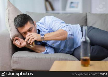 alcoholism, alcohol addiction and people concept - male alcoholic lying on sofa and drinking whiskey. alcoholic lying on sofa and drinking whiskey. alcoholic lying on sofa and drinking whiskey