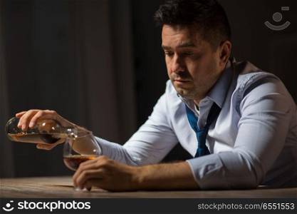alcoholism, alcohol addiction and people concept - male alcoholic pouring brandy from bottle to glass at table at night. drunk man drinking alcohol at table at night. drunk man drinking alcohol at table at night