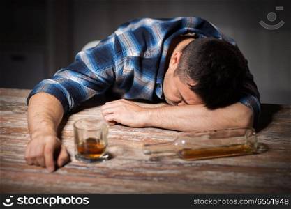 alcoholism, alcohol addiction and people concept - male alcoholic with glass of whiskey and bottle lying or sleeping on table at night. drunk man with glass of alcohol on table at night. drunk man with glass of alcohol on table at night