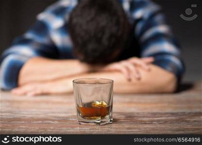 alcoholism, alcohol addiction and people concept - male alcoholic with glass of whiskey lying or sleeping on table at night. drunk man with glass of alcohol on table at night