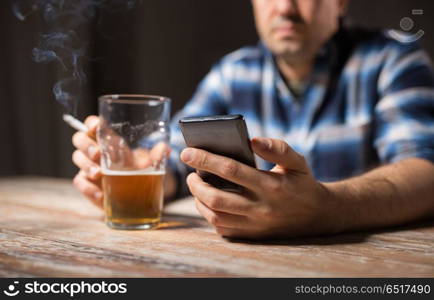 alcoholism, alcohol addiction and people concept - male alcoholic with smartphone drinking beer and smoking cigarette at night. man with cellphone drinking alcohol and smoking. man with cellphone drinking alcohol and smoking