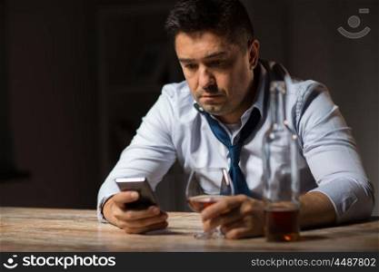 alcoholism, alcohol addiction and technology concept - male alcoholic with smartphone and glass of brandy at night. drunk man with smartphone and alcohol at night. drunk man with smartphone and alcohol at night