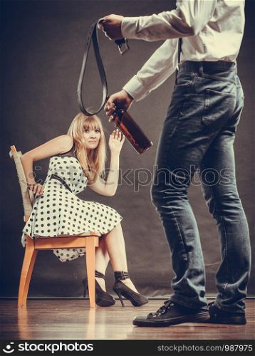 Alcoholism and violence problem. Man alcoholic holding bottle beating his scared wife with belt. Woman is victim of domestic abuse.