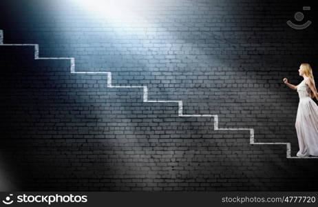 Alice in wonderland. Young woman in white long dress stepping up the staircase