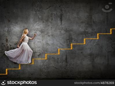 Alice in wonderland. Young woman in white long dress stepping up the staircase