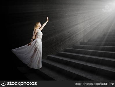 Alice in wonderland. Young woman in white long dress stepping up the staircase