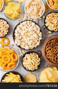 All classic potato snacks with peanuts, popcorn and onion rings and salted pretzels in bowl plates on light table. Twirls with sticks and potato chips and crisps with nachos and cheese balls.