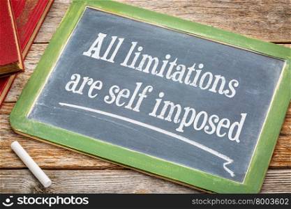all limitations are self imposed - inspirational statement on a blackboard with a white chalk and a stack of books against rustic wooden table