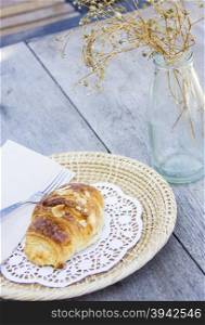 Almond croissant on wood table and dry flower in glass bottle