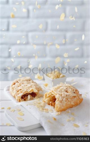 Almond flakes falling from above over caramel strudel on white brick background