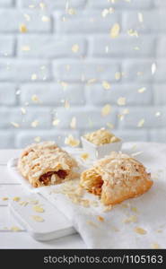 Almond flakes falling from above over caramel strudel on white brick background