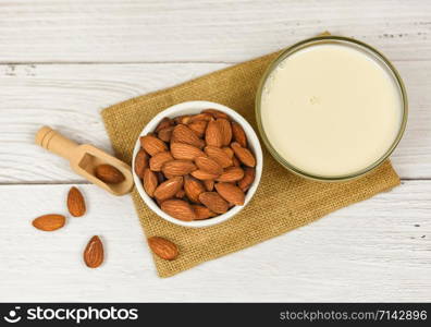 Almond milk in bowl and almonds on wooden scoop on sack background