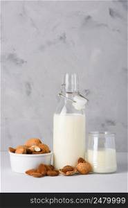 Almond milk in glass and bottle with whole organic almonds on table