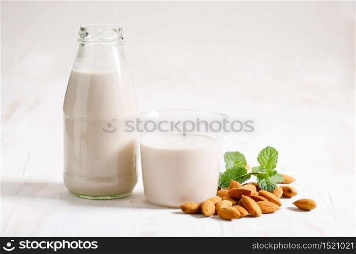 Almond milk in glass bottle with fresh almond nuts on white wooden background