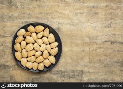 almond nuts in shells on a black plate against textured bark paper with a copy space
