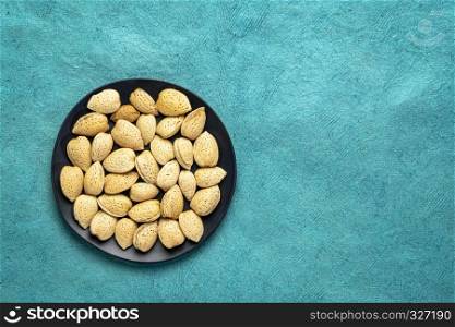 almond nuts in shells on a black plate against turquoise bark paper with a copy space