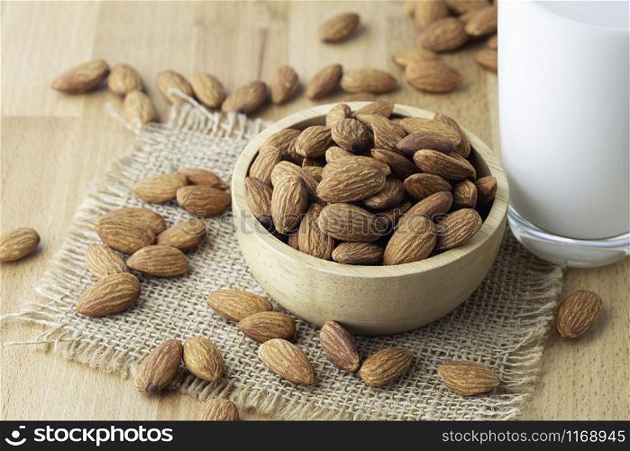 Almond seeds in a bowl wood on the sackcloth And a glass of milk on table wooden background