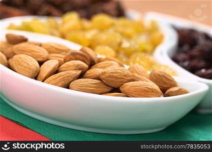 Almonds, sultanas and raisins in small bowls on red and green napkins (Selective Focus, Focus on the almonds in the front). Almonds and Raisins