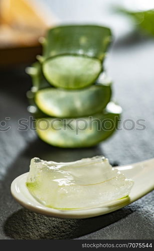 Aloe vera slices on dark background and spoon with aloe gel. Health and beauty concept. Closeup aloe pieces on backlight.