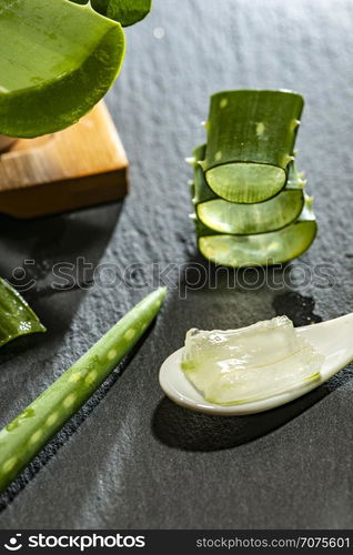 Aloe vera slices on dark background and spoon with aloe gel. Health and beauty concept. Closeup aloe pieces on backlight.