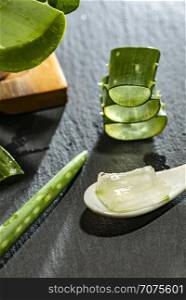 Aloe vera slices on dark background and spoon with aloe gel. Health and beauty concept. Closeup aloe pieces on backlight.