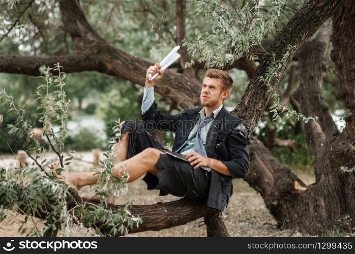 Alone businessman in torn suit resting on the tree on lost island. Business risk, collapse or bankruptcy concept. Alone businessman resting on the tree, lost island