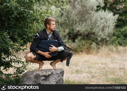 Alone businessman in torn suit sitting on the stone on lost island. Business risk, collapse or bankruptcy concept