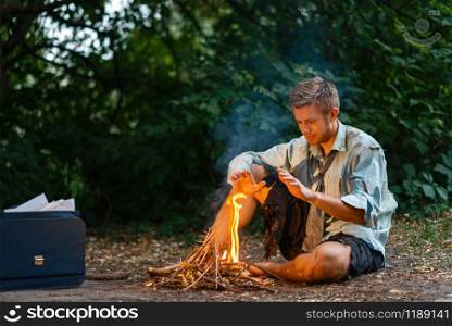 Alone businessman warms by the fire on lost island. Business risk, collapse or bankruptcy concept