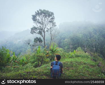 Alone man hiking enjoyment the morning mist in lush tropical rainforest.