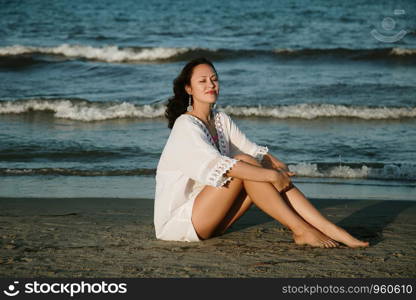 Alone sensual woman sitting on the beach in a light summer dress