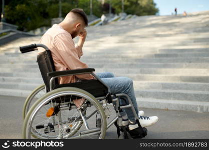 Alone young man in wheelchair at the stairs, handicap problem. Paralyzed people and disability, handicap overcoming. Helpless disabled male person walking in park. Man in wheelchair at the stairs, handicap problem