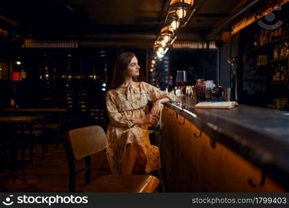 Alone young woman with glass of red wine sitting at the counter in bar. One female person in pub, human emotions, leisure activities. Alone woman with glass of wine sitting in bar