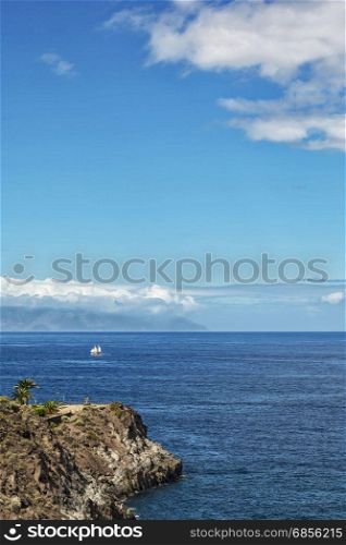 Along the rocky shore a sailboat sails with white sails